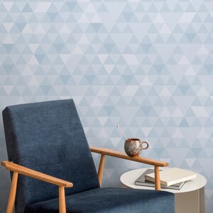Può includere: Una poltrona blu con braccioli e gambe in legno si trova di fronte a un muro con un motivo geometrico blu chiaro. Un tavolino con una tazza in ceramica marrone e un mestolo di legno si trova di fronte alla poltrona.