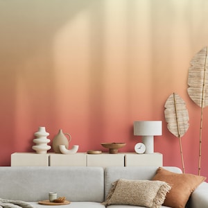 Könnte beinhalten: Wohnzimmerszene mit einer Wand in Pfirsich- und Cremefarben. Ein weißer Schrank beherbergt dekorative Vasen, eine Lampe und eine Uhr. Im Vordergrund befindet sich ein graues Sofa mit orangefarbenen Kissen und einer gewebten Decke.