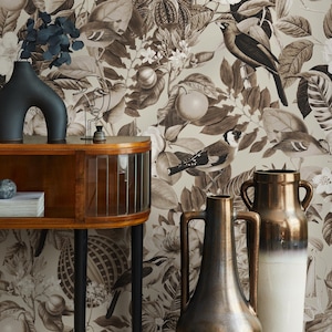 Könnte beinhalten: Eine dekorative Szene mit einem Holzschrank, schwarzen Vasen und einer floralen Tapete. Die Tapete zeigt Vögel, Blätter und Früchte in Braun- und Weißtönen. Eine Metallskulptur und Bücher befinden sich auf dem Schrank.
