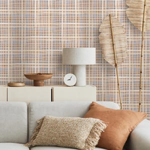 Könnte beinhalten: Ein Wohnzimmer mit einem hellgrauen Sofa und dekorativen Kissen in Beige- und Orangetönen. Eine Holzschale und eine weiße Uhr stehen auf einem cremefarbenen Schrank. Die Tapete hat ein Gittermuster in Beige, Blau und Braun.