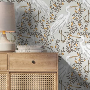 May include: A light gray wallpaper featuring a repeating pattern of white herons and branches with yellow berries. The herons are depicted in a graceful pose, and the branches have dark gray leaves. The wallpaper has a soft, muted color palette.