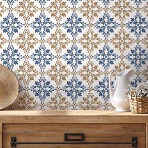 May include: A decorative wall with a repeating pattern of blue and tan floral designs on a white background. A white pitcher, a basket of flowers, and a straw hat sit on a wooden surface.