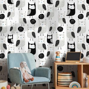 May include: White wallpaper featuring a repeating pattern of owls in black, grey, and white. The owls have large eyes and are surrounded by black circles. A light blue armchair and a stuffed bunny are in the foreground.