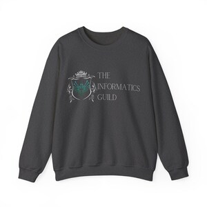 Peut inclure: Sweat-shirt gris foncé avec le texte "THE INFORMATICS GUILD" et un blason. Le blason présente une couronne, un bouclier avec un motif de circuit imprimé turquoise et blanc, et des ornements. Vêtement décontracté à manches longues.