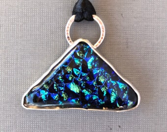 May include: A silver pendant with a triangular shaped piece of dichroic glass. The glass is iridescent and has shades of blue, green, and black.