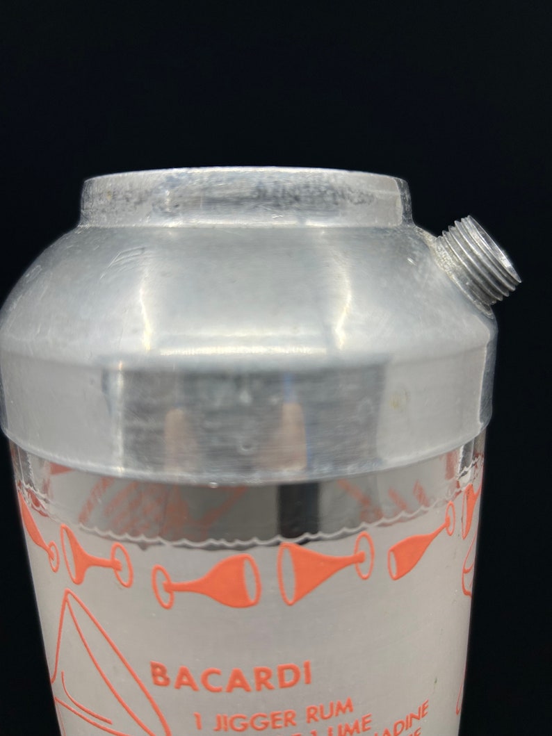 Puede incluir: Coctelera de plata con fondo de vidrio y un logotipo de Bacardi rosa e instrucciones. La coctelera tiene una tapa de rosca y un pico de vertido.