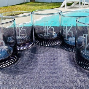 May include: Set of five clear glass tumblers with a black base. Each tumbler has a different letter etched into the glass.