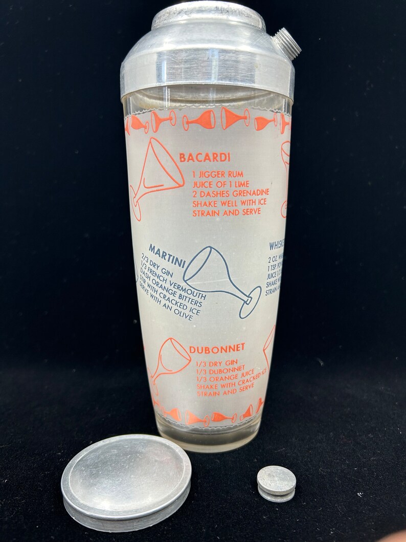 Puede incluir: Un coctelera de plata con un inserto de vidrio que presenta recetas de c&oacute;cteles Bacardi, Martini y Dubonnet. La coctelera tiene una tapa de plata y una base de plata.