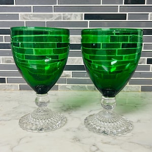 Puede incluir: Dos copas de vino verde esmeralda con un diseño de ladrillos en el cuenco. Los tallos son transparentes con una base redonda y un pie circular texturizado. Sobre un fondo de azulejos grises y blancos.