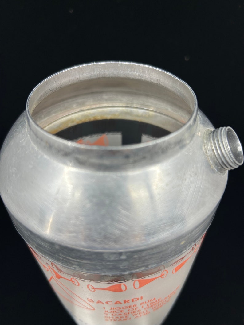 Puede incluir: Una coctelera de plata con una banda negra y una etiqueta blanca con texto rojo. La etiqueta dice "Bacardi Rum 1 jigger de Bacardi Rum 1 jigger de jugo de lima 2 pizcas de granadina Agitar bien Colar y servir"