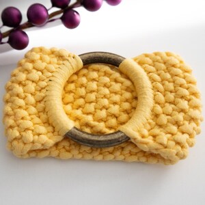 May include: A yellow crocheted ring with a wooden ring in the center. The ring is made of a soft, textured yarn.