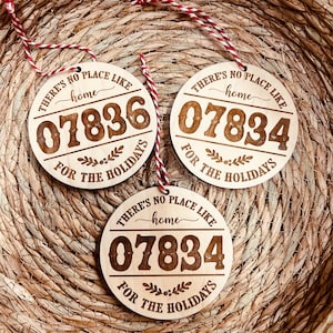 May include: Three round wooden ornaments with the text "There's no place like home" and the number "07834" with the words "For the Holidays" below. The ornaments are hanging from red and white string.
