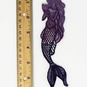 May include: Purple and black lace mermaid applique with a detailed design. The mermaid is holding a seashell in her hand. The applique is approximately 5 inches tall.