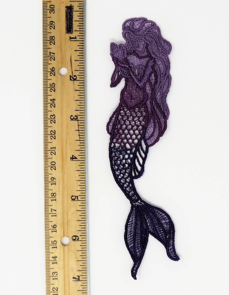 May include: Purple and black lace mermaid applique with a detailed design. The mermaid is holding a seashell in her hand. The applique is approximately 5 inches tall.