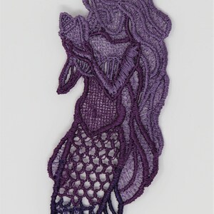 May include: Purple lace applique with a mermaid design. The lace is a gradient of purple shades, with a darker purple at the bottom and a lighter purple at the top.