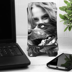 May include: Black and white photo of a woman and a dog. The woman is leaning down and the dog is looking up at her. The photo is printed on a phone stand.