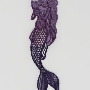 May include: Purple and lavender embroidered mermaid applique with a detailed design. The mermaid is holding a seashell in her hand and has long flowing hair.