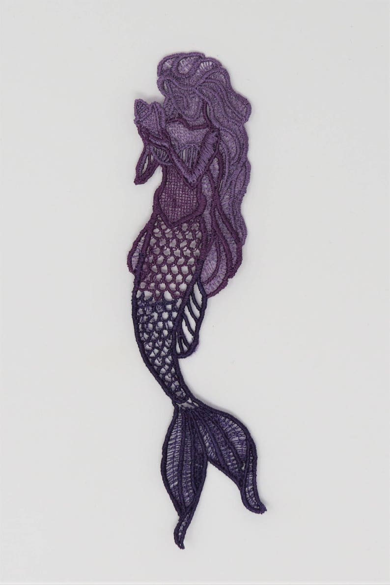 May include: Purple and lavender embroidered mermaid applique with a detailed design. The mermaid is holding a seashell in her hand and has long flowing hair.