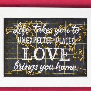 May include: White framed chalkboard with a gold and white embroidered quote: "Life takes you to unexpected places, love brings you home."
