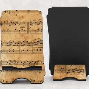 May include: A wooden phone stand featuring a vintage sheet music design. The stand has a black support and a slot to hold a phone. The front of the stand displays musical notes on a tan background.