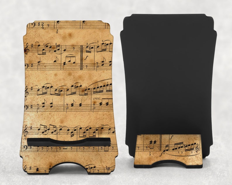 May include: A wooden phone stand featuring a vintage sheet music design. The stand has a black support and a slot to hold a phone. The front of the stand displays musical notes on a tan background.