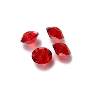 Könnte beinhalten: Vier rote Kristallperlen mit facettiertem Design. Die Perlen sind klein und haben eine glänzende Oberfläche.