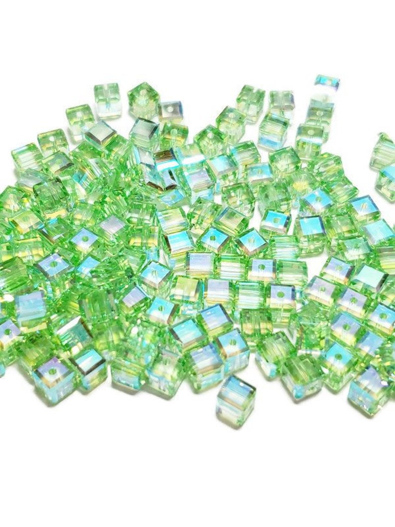 May include: A large pile of light green square glass beads with iridescent facets. The beads have a hole in the center for stringing.