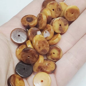 May include: A pile of brown and yellow round beads with a hole in the center. The beads are made of a marbled material and have a natural, rustic look.
