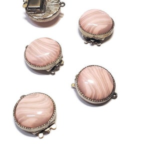 May include: Five silver-toned metal clasps with pink and white swirl patterned glass inserts. Each clasp has a decorative edge and a loop for attaching to a necklace or bracelet.