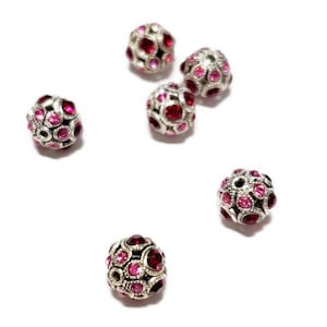 May include: Six silver-toned round beads with pink rhinestones. The beads have a decorative design and are perfect for jewelry making.