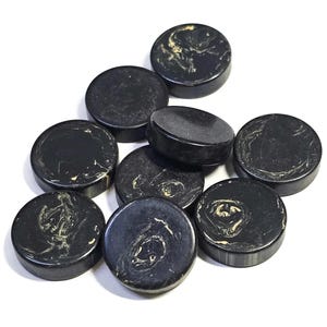 May include: A collection of nine circular buttons featuring a black base with swirling white and cream marbled patterns. Each button has a smooth, polished surface and a flat, cylindrical shape, displaying unique organic veining throughout.