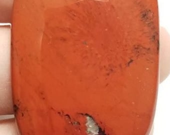 Puede incluir: Un colgante de jaspe rojo con un agujero perforado en la parte superior. El colgante tiene forma rectangular y una superficie lisa y pulida.
