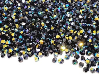 Puede incluir: Un montón de cuentas negras facetadas con reflejos iridiscentes amarillos, azules y verdes. Las cuentas están dispersas sobre un fondo blanco, creando un efecto brillante. Adecuadas para la fabricación de joyas y manualidades.