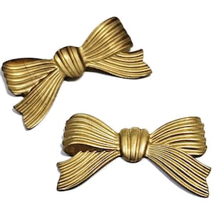May include: Two gold-colored metal bow embellishments. The bows are made of a textured metal and have a three-dimensional shape.