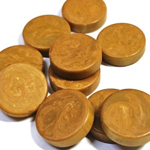 May include: A collection of ten circular, flat-topped buttons in a warm, golden-brown hue. Each button features a smooth, polished surface with subtle, swirling marbled patterns in lighter and darker shades of brown throughout the material.