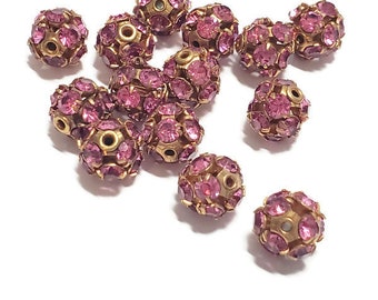 May include: A scattering of pink rhinestone beads with gold settings. The beads are round and have a faceted design.