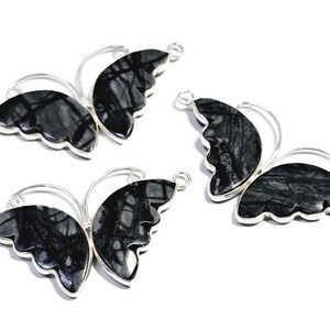 May include: Three silver butterfly charms with black and white stone inlays. The charms have a loop on each side for attaching to jewelry.