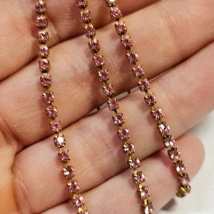 May include: Three strands of pink rhinestone chain with gold metal connectors.