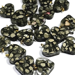 May include: A collection of 15 heart-shaped charms made of clear resin with black and gold flecks. The charms have a gold loop at the top for attaching to jewelry or other crafts.