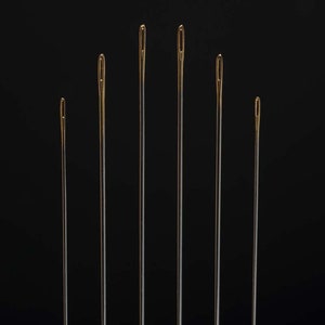 May include: Seven gold-tipped needles of varying lengths against a black background.
