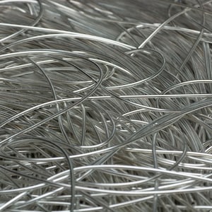 May include: Close-up of a tangled mass of silver-coloured wire. The wires are curved and intertwined, creating a dense, textured pattern. The metallic material reflects light, highlighting the curves and the overall shape of the wire.
