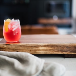May include: A glass of red cocktail with ice and a lemon wedge on a wooden serving board.