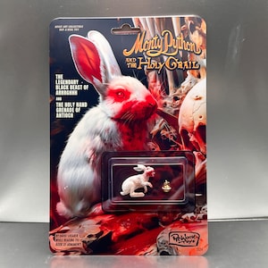 May include: A white rabbit figurine with red blood splatters, packaged in a plastic blister pack. The packaging features a graphic of a bloody rabbit with the text "Monty Python and the Holy Grail".