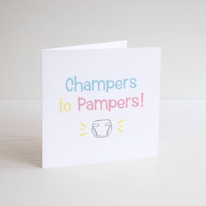 May include: A white card with the text "Champers to Pampers!" in blue, pink, and yellow. A simple drawing of a nappy is below the text.