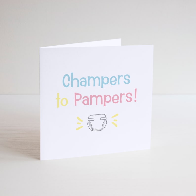 May include: A white card with the text "Champers to Pampers!" in blue, pink, and yellow. A simple drawing of a nappy is below the text.