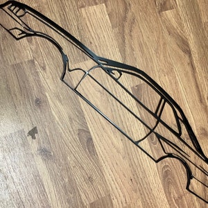 Può includere: Un contorno di auto in metallo nero, probabilmente una decorazione da parete. Il design presenta il profilo laterale di un'auto, con dettagli di finestre, porte e carrozzeria. Posizionato su una superficie di legno.