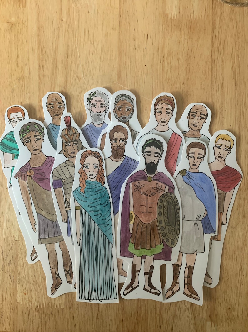 May include: A set of 12 paper cut-outs of people in various poses and clothing. The figures are drawn in a cartoon style and are all wearing different outfits, including a toga, a tunic, and a dress. The figures are all standing on a wooden surface.