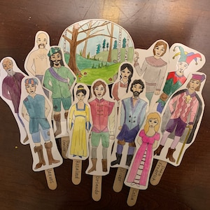 Peut inclure: Un ensemble de 11 illustrations de personnages peintes à la main sur des bâtonnets en bois. Les personnages sont habillés de costumes variés et ont des expressions faciales différentes. Les illustrations sont sur fond de scène de forêt.
