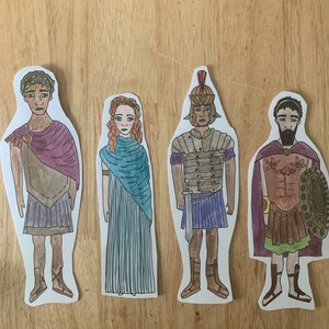 May include: Four paper dolls depicting Roman figures. The figures are wearing traditional Roman clothing, including tunics, togas, and armour. The dolls are hand-drawn and coloured in a cartoon style.