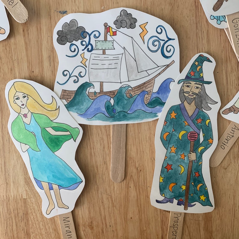 May include: A set of three paper puppets depicting characters from a play. The puppets are on sticks and feature a woman with blonde hair, a man with a beard and a wizard's hat, and a ship sailing through stormy seas.